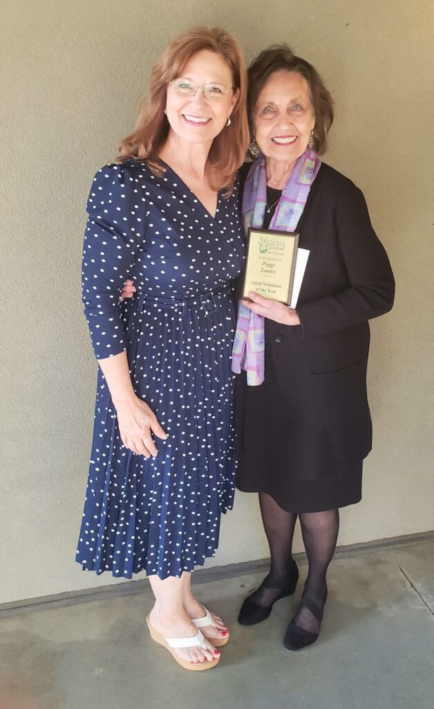 Two ladies standing with one holding a Magnolia Festival volunteer award plaque.