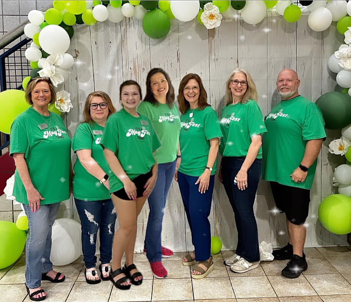 Seven men and women wearing green Magnolia Festival t shirts at a selfie station. 